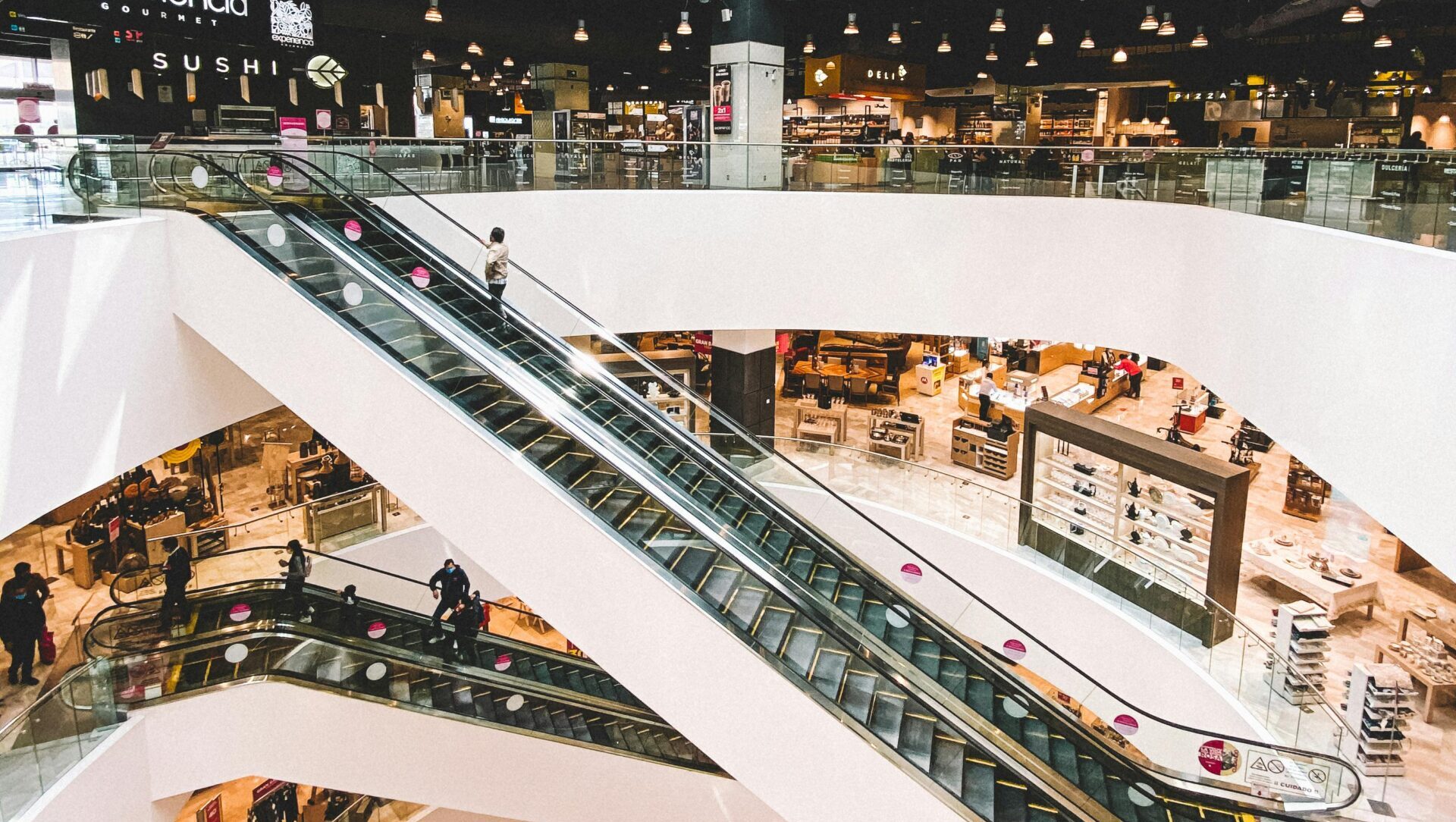 A bustling modern shopping mall with multiple escalators and retail shops in Toluca de Lerdo, Mexico.
