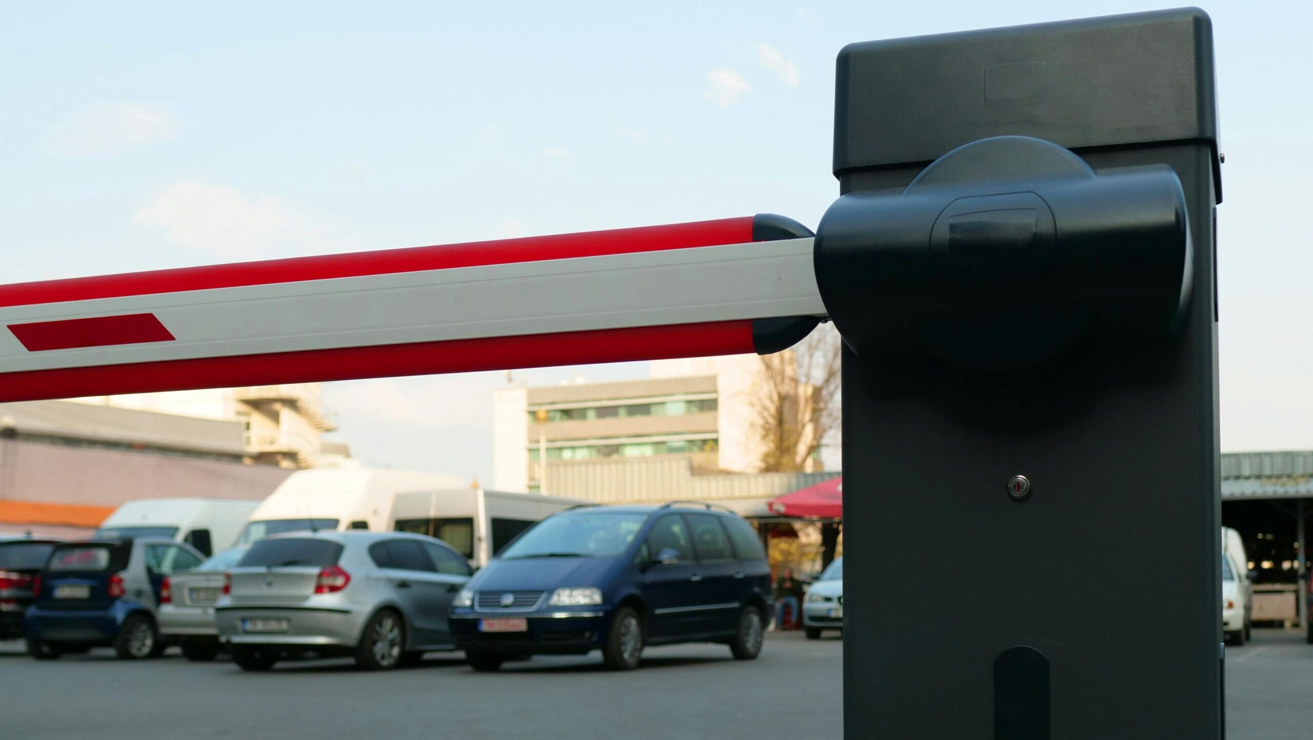 Close-up of a parking lot barrier gate with vehicles in the background, modern and automated.
