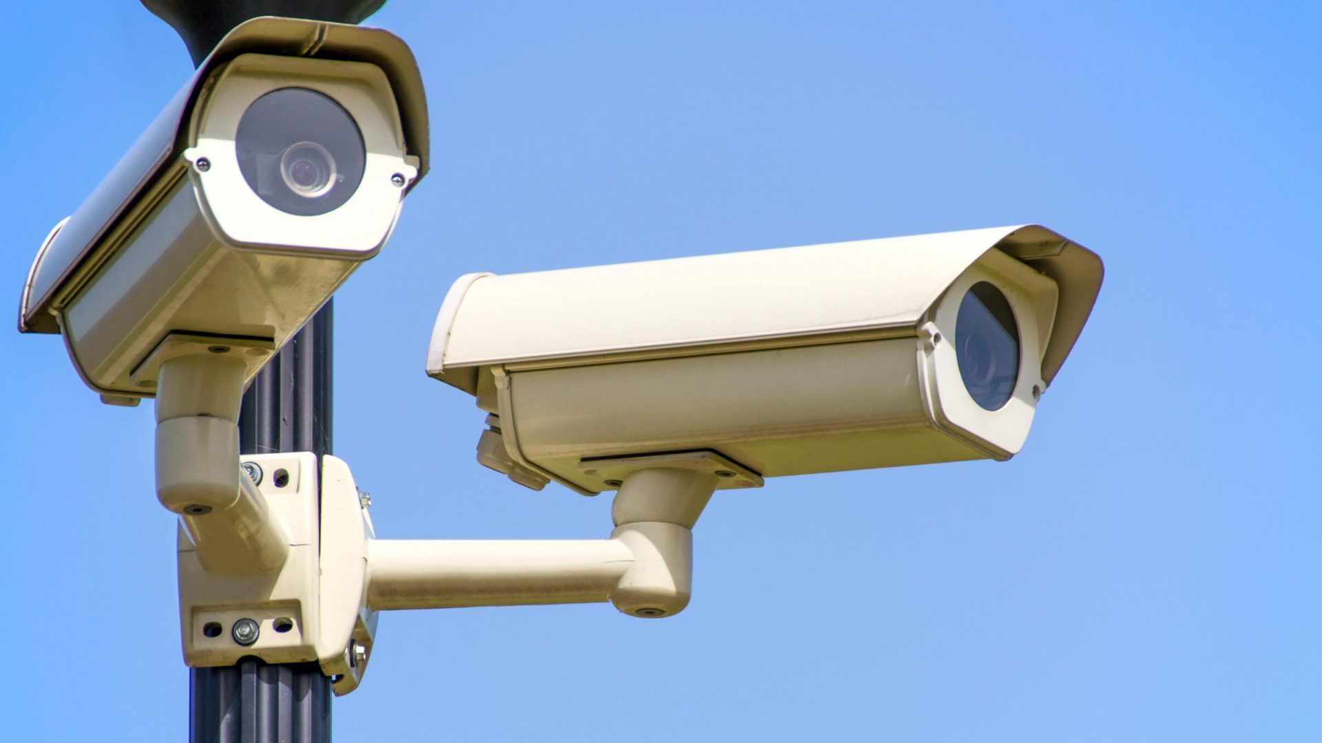 Outdoor security cameras mounted on a pole against a clear blue sky, ensuring vigilant surveillance.